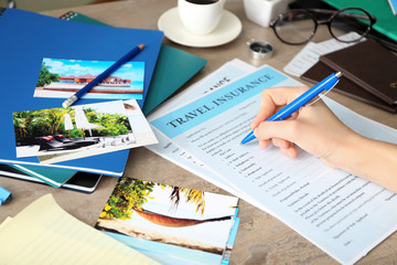 Woman filling in blank travel insurance form on table