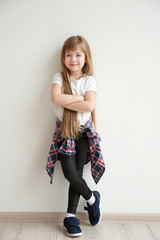 Cute little girl on light wall background. Fashion concept