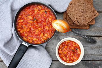 Stew pan and bowl with delicious Italian butter beans on wooden background