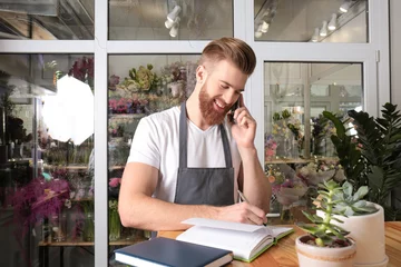 Crédence de cuisine en verre imprimé Fleuriste Jeune beau fleuriste écrivant une commande tout en parlant par téléphone portable dans un magasin de fleurs