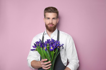 Young handsome florist with beautiful bouquet on pink background