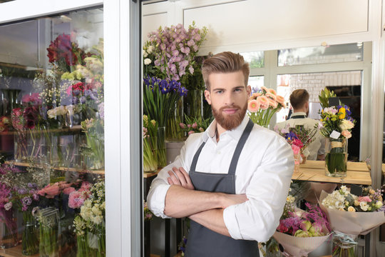 Portrait of young handsome florist with crossed arms in flower shop
