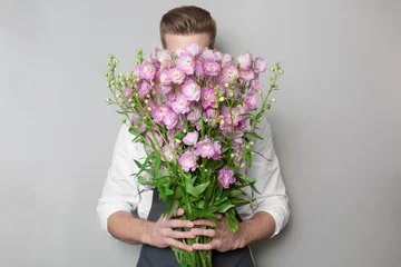 Photo sur Plexiglas Fleuriste Young florist hiding behind beautiful bouquet on grey background