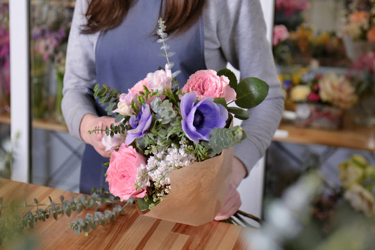 Female florist packing beautiful bouquet in wrapping paper at flower shop