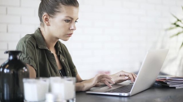 Side view of a beautiful young woman typing at her laptop and using a touchpad in an office. Tilt upl real time medium shot