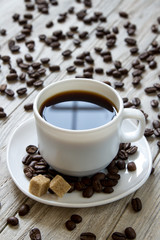 Black coffe in a white cup and cane sugar on a plate on wooden background