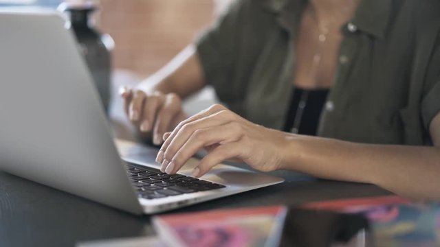 Close up of woman s hands typing at her laptop keyboard and using a touchpad in an office. Right to left pan real time close up shot
