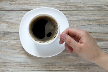 Female hand hold a cup of black coffee on wooden background