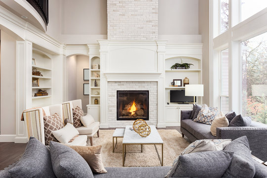 Beautiful Living Room in New Luxury Home with Fireplace and Roaring Fire. Large Bank of Windows Hints at Exterior View
