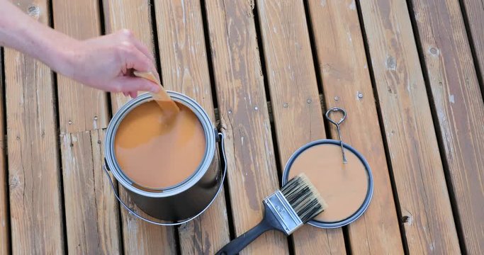 Footage of hand stirring wood stain in a can on a natural cedar wooden deck 