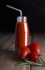 Tomato red juice in a glass bottle with fresh tomatoes, a sprig of rosemary and sea salt on a wooden old table on a black background. Side view. Сopy place. Mock up. Vegetable.