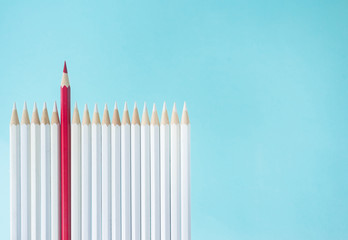 Business concept - lot of white pencils and one color pencil stand on blue paper background like fence. It's symbol of leadership, teamwork, united and communication.