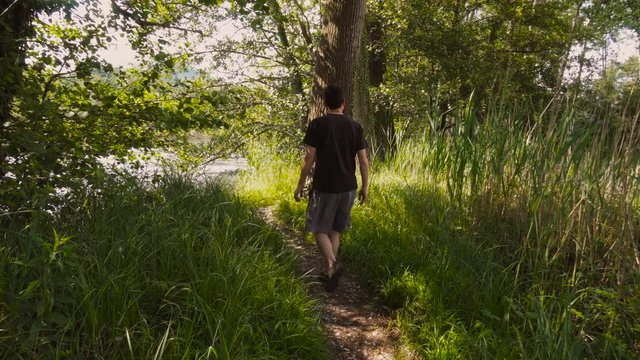 Young Man Walking on a Footpath Towards the Lake in Summer