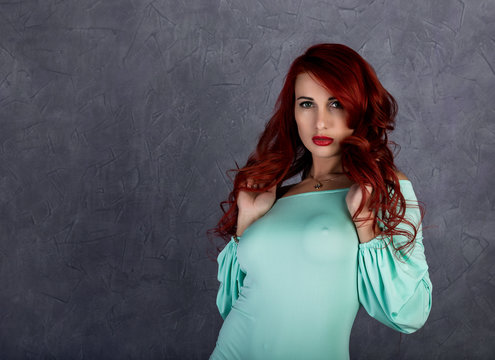 sexy beautiful redhead young woman with big boobs in a turquoise dress on a gray background