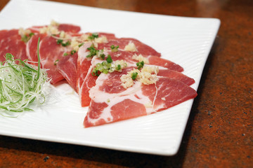 Raw Sliced Kurobuta Pork with salt and garlic on white plate, Prepared for Japanese Barbecue Style called Yakiniku.