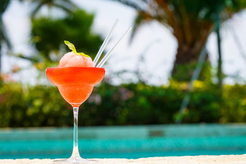 Frozen strawberry margarita cocktail at the edge of a resort pool.  Concept of luxury vacation