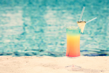Rainbow cocktail at the edge of a resort pool.  Concept of luxury vacation - obrazy, fototapety, plakaty