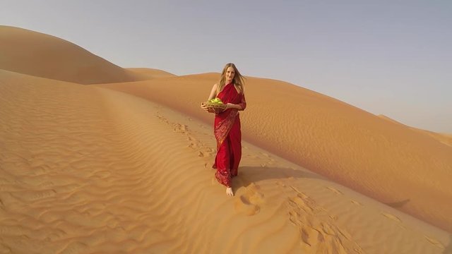 woman in red sari in Liwa desert with a bowl of apples