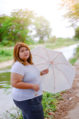 portrait asian beautiful fat woman with umbrella in the garden, relax in the garden, Large woman happy in the meadow, Woman with overweight, beautiful plus size. Asian girl with umbrella.