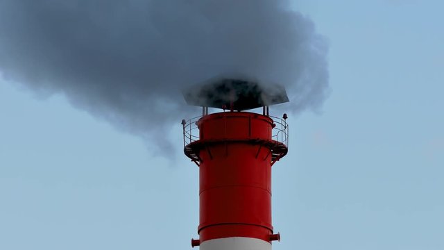 Chimney smoke / Smoke stack / Air pollution. Smoke comes from red-white chimney on thermoelectric plant against sky.