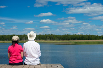 Fototapeta na wymiar Man and woman are sitting on the shore and looking at a beautiful lake