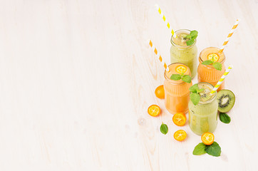 Freshly blended orange kumquat and green kiwi fruit smoothie in glass jars with straw, mint leaf, cut ripe berry, copy space. White wooden board background.