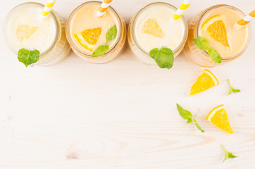 Freshly blended orange and yellow lemon smoothie in glass jars with straw, mint leaf,   slices orange and lemon, top view. White wooden board background, copy space.