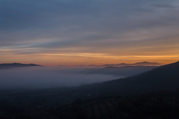 View from above of a valley filled by fog at sunset