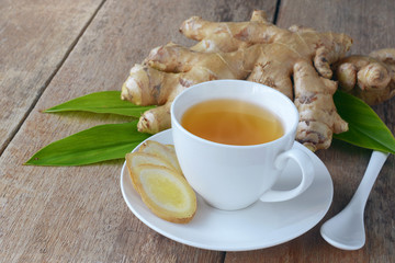 cup of ginger tea with sliced root on wooden table.