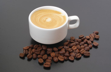 White cup of coffee with roasted coffee beans on dark table
