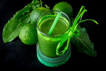 Green smoothie near centimeter and  ingredients for it on black wooden background. Diet. Detox. Healthy drink.