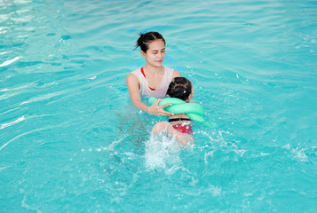 happy smiling asian little girl with mother swimming at water pool.