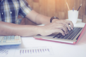 Close up of hand of hipster working man typing a keyboard of notebook, Asian business male using a laptop for calculate finance data on a desk with a wooden wall