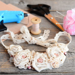 Casual floral fabric necklace, glue hot gun, scissors, thread, needle, felt on a vintage wooden table. Creating a flowers jewelry using vintage and recycled cotton fabrics, beads and felt 