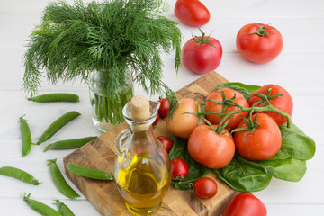 Olive oil, parsley, spinach, green peas and a branch of tomatoes on a white background