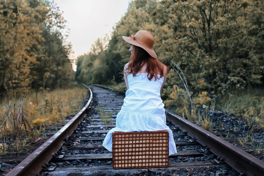 autumn park girl in white sundress and a wicker suitcase walking on rails