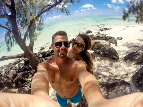 Beautiful young couple taking a selfie on the beach, enjoying their honeymoon. Turquoise ocean water in the background.  on the beach. Turquoise ocean water in the background.