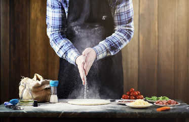 man in an apron preparing a pizza, knead the dough and puts ingredients