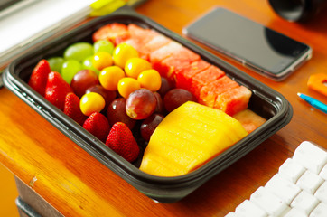 Close up of a healthy breakfast, fruit salad packed in plastic box on wooden table