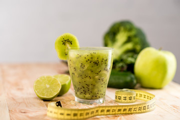 fresh fruit smoothie in glass with piece of kiwi, limes and measuring tape on tabletop
