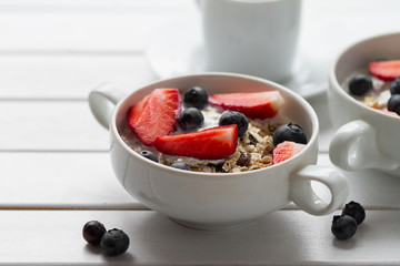 Tasty colorful Breakfast with Oatmeal, Yogurt, Strawberry, Blueberry, Honey and Milk on White Wooden Background with Copy Space. Closeup.
