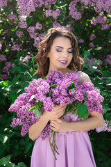 Beautiful young woman with bouquet of lilac in spring garden
