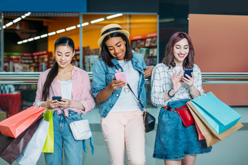 Smiling young women with shopping bags using smartphones, young girls shopping concept