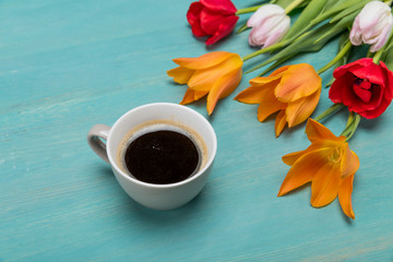 Close-up view of beautiful tender tulips with green leaves and cup of coffee on blue wooden table top