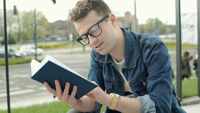 Young man looks happy after finished reading book, steadycam shot
