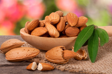 heap of peeled almonds with leaf in a wooden spoon on table blurred garden background