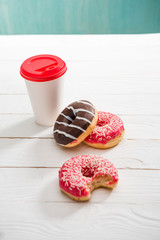 High angle view of coffee cup and three donuts with chocolate and raspberry icing. donuts and coffee concept