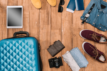 Summer vacation background with travel accessories. closed luggage, shoes, digital devices and passports on wooden floor.