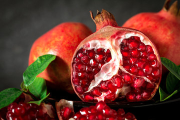 Fresh red pomegranate and seed  with leaves over black stone background