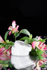 face cream in plastic jar with flowers in water, natural cosmetic concept